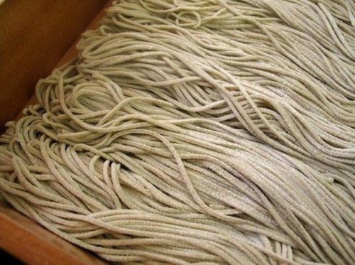 A close-up of a pile of thin, light-colored noodles arranged neatly in a wooden container.