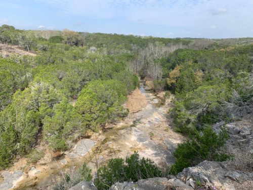 A scenic view of a lush green landscape with a winding creek and rocky terrain under a clear sky.