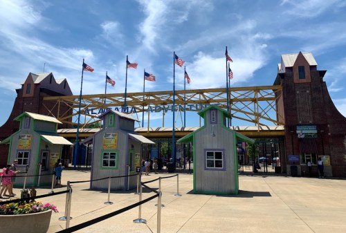 Entrance to Alabama Adventure amusement park, featuring colorful ticket booths and flags under a blue sky.