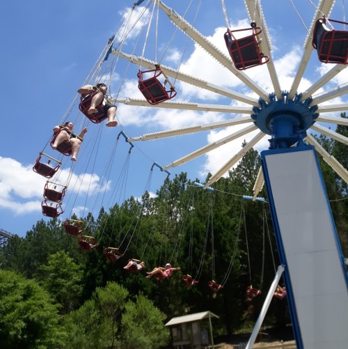 A swing ride with several people enjoying the view against a blue sky and green trees in the background.