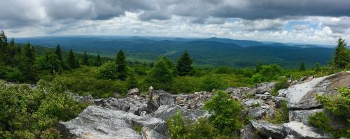 A panoramic view of a lush green landscape with rocky outcrops and cloudy skies in the distance.
