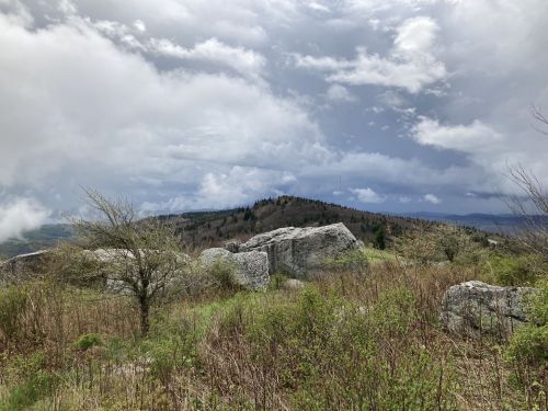 A scenic view of rocky terrain with green vegetation under a cloudy sky and distant hills.