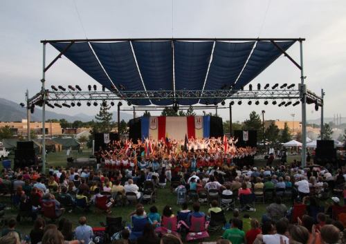 A large outdoor stage with performers and flags, surrounded by an audience seated on the grass.