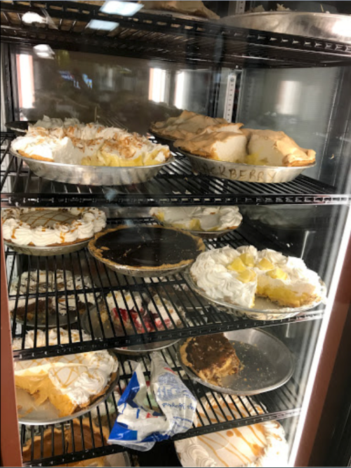 A display case filled with various pies, including cream and fruit varieties, on multiple shelves.