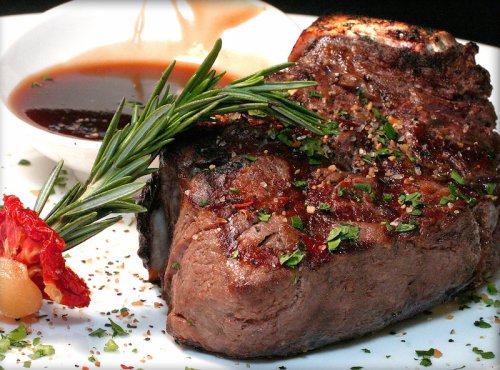 A perfectly cooked steak garnished with herbs, served with a side of sauce and a decorative slice of tomato.