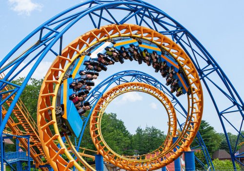 A roller coaster with riders upside down, featuring vibrant blue and orange loops against a clear sky.
