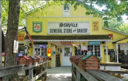 A bright yellow general store and bakery with a wooden walkway, featuring colorful birdhouses and a coffee sign.