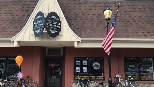 Exterior of Kalona Chocolates shop with bicycles parked outside, an American flag, and a balloon in front.