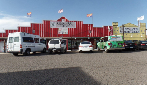 A colorful general store on Route 66, with several parked vehicles in front and flags waving above.