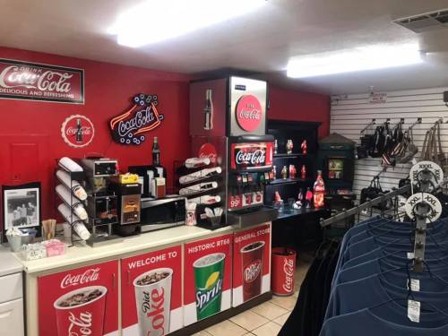 A vintage-style general store display featuring Coca-Cola merchandise, drinks, and apparel in a cozy setting.
