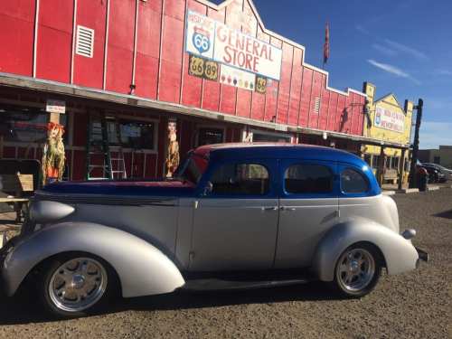 A vintage silver and blue car parked in front of a colorful general store on Route 66.