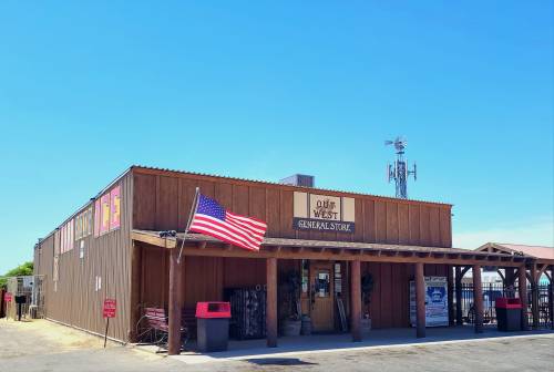 A wooden general store with an American flag, under a clear blue sky, featuring a windmill in the background.