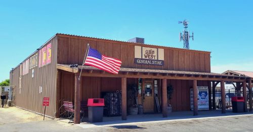 A rustic wooden general store with an American flag, set against a clear blue sky.