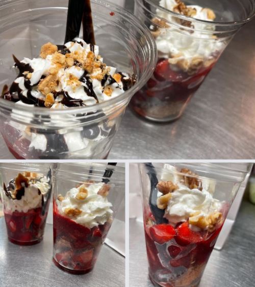 Two clear cups filled with layers of strawberries, whipped cream, chocolate sauce, and crushed nuts.