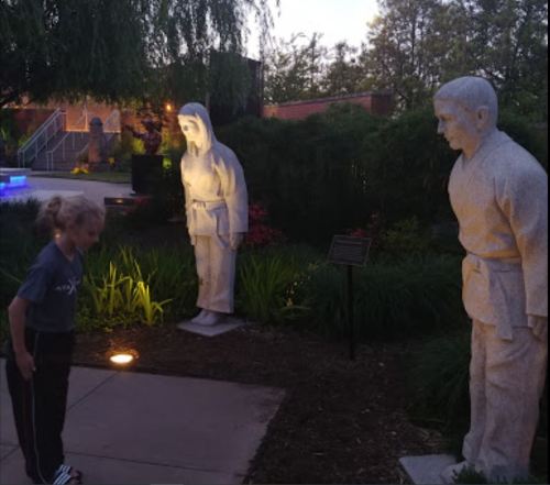 A child stands in front of two illuminated stone statues in a garden at dusk.