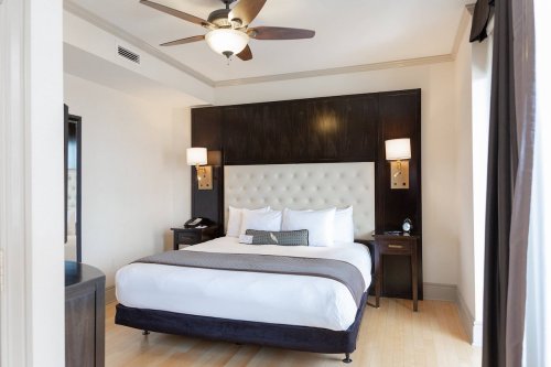 A modern hotel room featuring a large bed, nightstands, a ceiling fan, and light-colored walls.