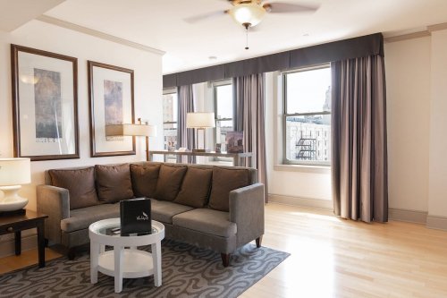 A cozy living room with a gray sofa, round coffee table, and large windows dressed with curtains.