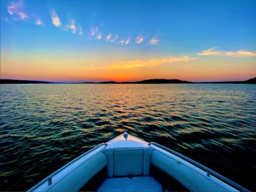 A boat's bow facing a tranquil lake at sunset, with vibrant colors reflecting on the water.