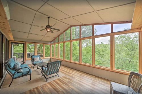 Bright sunroom with large windows, wooden ceiling, and comfortable seating overlooking lush greenery.