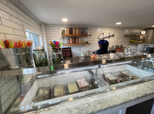 A cozy ice cream shop interior with a display case, colorful spoons, and a staff member behind the counter.