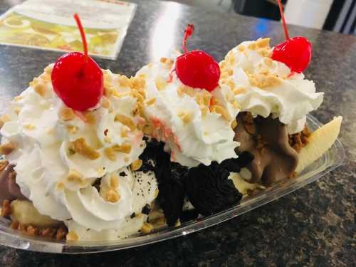 A delicious banana split topped with whipped cream, nuts, and cherries, served in a clear dish on a dark countertop.