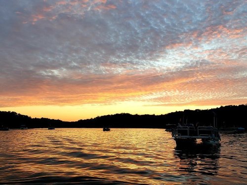 A serene lake at sunset, with colorful clouds reflecting on the water and boats gently floating.