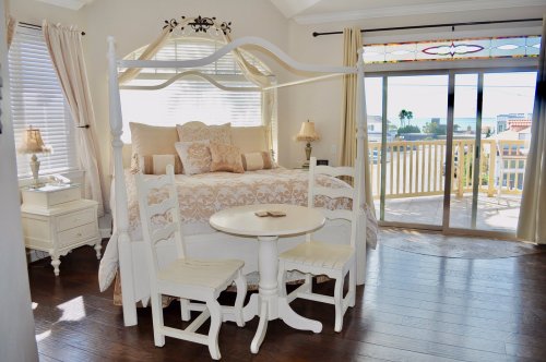 Bright bedroom featuring a four-poster bed, a small table with two chairs, and large windows with a view.