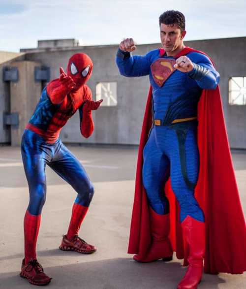 Two superheroes pose on a rooftop: one in a Spider-Man costume and the other in a Superman outfit with a cape.