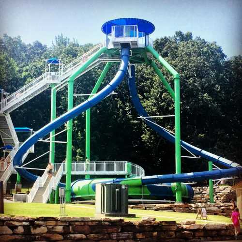 A large water slide structure with multiple twisting slides and a tower, set in a green park area.