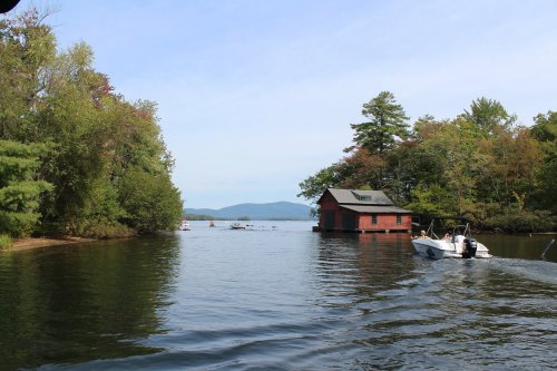 A serene lake scene with a red boathouse, surrounded by trees and mountains, as a boat glides through the water.