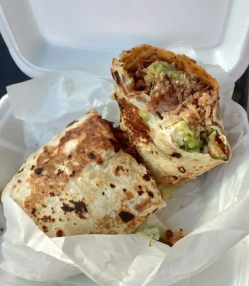A partially eaten burrito wrapped in paper, revealing rice, beans, and guacamole inside.