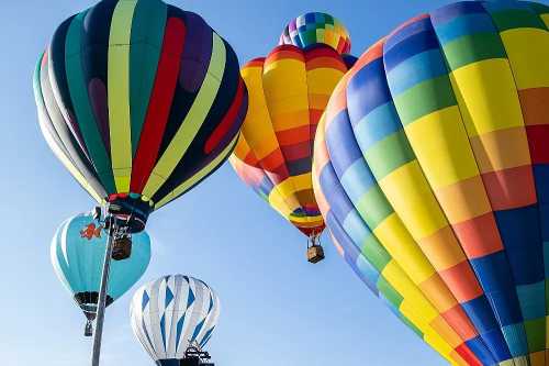 Colorful hot air balloons in various patterns floating against a clear blue sky.