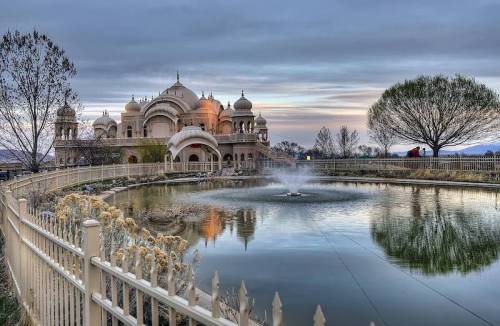 A serene temple by a pond at sunset, with reflections in the water and trees in the background.