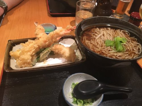 A bowl of soba noodles in broth next to a plate of tempura shrimp and vegetables, with green onions on the side.