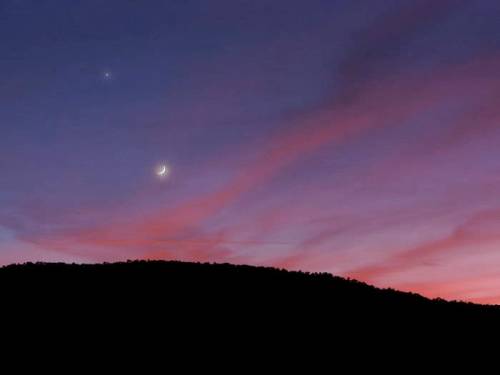 A serene twilight sky with a crescent moon and a bright planet above a dark silhouette of a mountain.