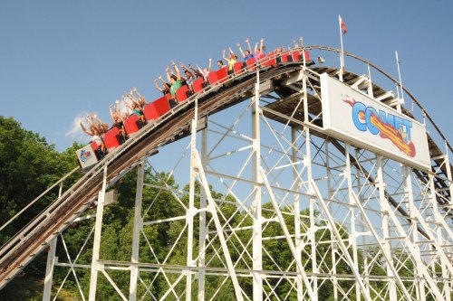 A roller coaster with riders raising their hands in excitement as it crests a hill against a clear blue sky.