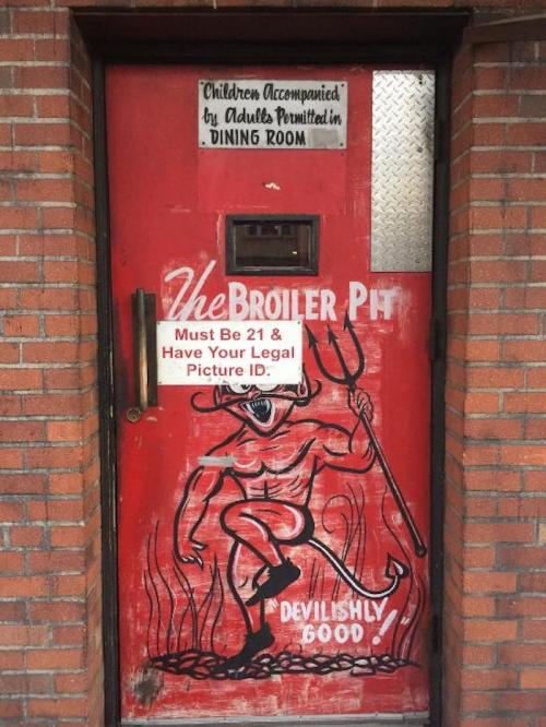 A red door with a devilish character illustration and signs about age restrictions and dining room rules.