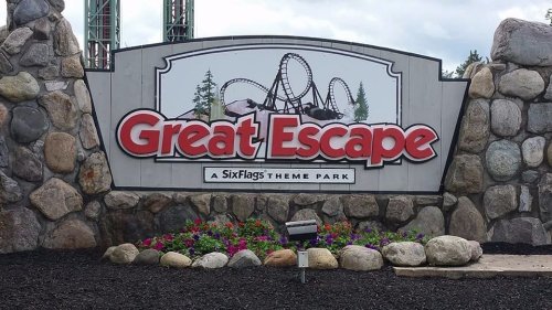 Sign for Great Escape, a Six Flags theme park, featuring a roller coaster design and surrounded by colorful flowers.