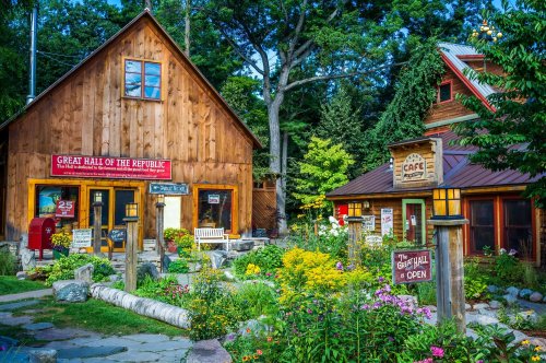 A charming wooden building with signs for "Great Hall of the Republic" and "Cafe," surrounded by colorful flowers and greenery.