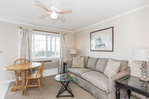 Cozy living area with a sofa, dining table, and large window, featuring light decor and a ceiling fan.