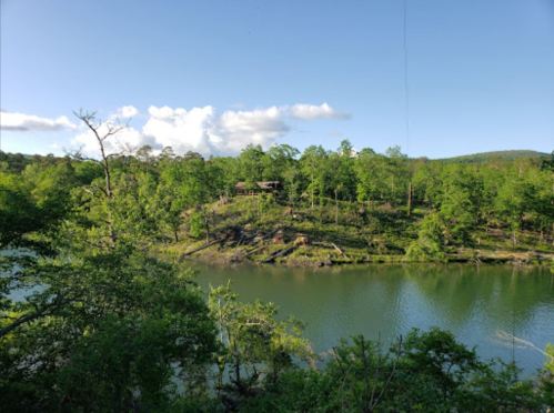 A serene landscape featuring a calm river surrounded by lush green trees and a clear blue sky.