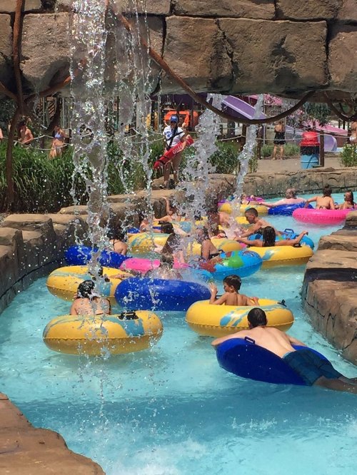 A water park scene with children floating on colorful inner tubes in a lazy river, surrounded by splashing water.
