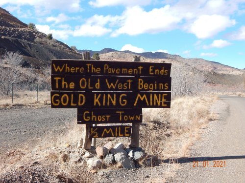A weathered wooden sign reads "Where The Pavement Ends, The Old West Begins, Gold King Mine, Ghost Town, ½ Mile."