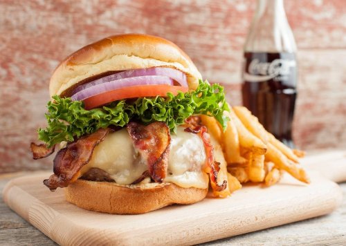 A delicious burger with bacon, cheese, lettuce, tomato, and onion, served with fries and a bottle of Coca-Cola.