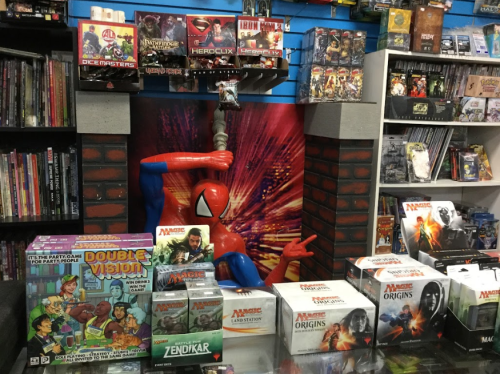 A display of board games and collectibles featuring Spider-Man in a comic shop, with various game boxes on shelves.