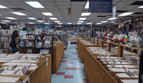 A comic book store interior with wooden display racks filled with comics and collectibles, and shelves lined with merchandise.