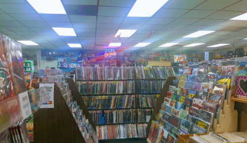 A spacious comic book store filled with shelves of comics and graphic novels, brightly lit with overhead lights.