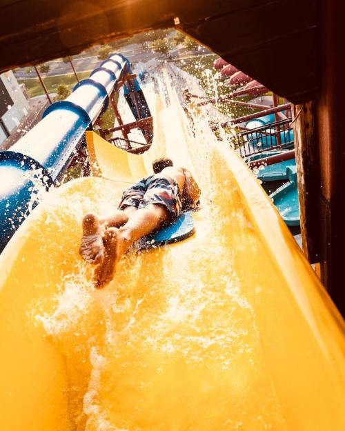 A person slides down a colorful water slide, splashing into the pool below on a sunny day.