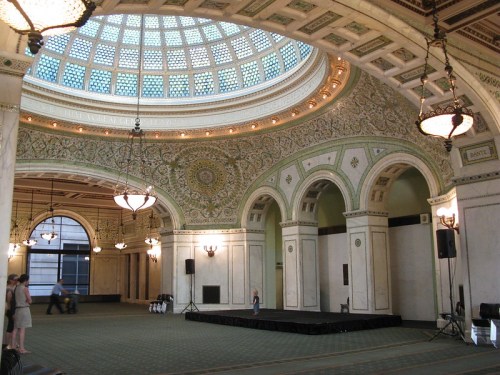 Interior of a grand hall with a domed ceiling, ornate decorations, and a stage set up for an event.