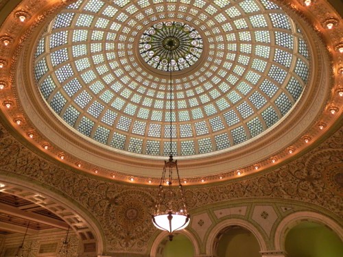 Intricate dome ceiling with a geometric pattern and decorative details, illuminated by a central chandelier.